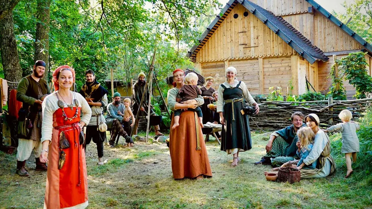 En grupp människor i vikingakläder samlas framför ett trädhus i vikingabyn Storholmen.