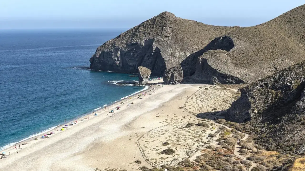 Sonnige Playa de los Muertos mit türkisfarbenem Meer, Felsen und vielen Sonnenanbetern.