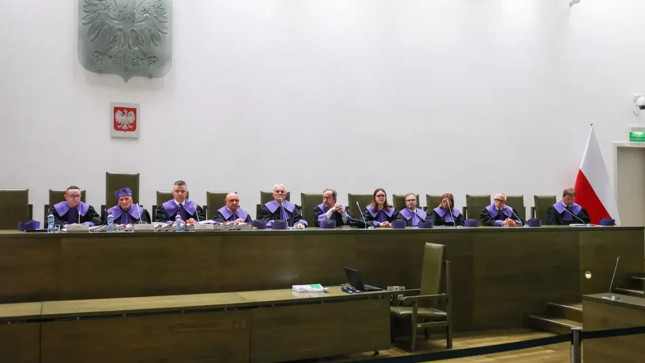 Sędziowie w togach siedzą za stołem w sali sądowej, przygotowując się do rozprawy przed trybunałem stanu.