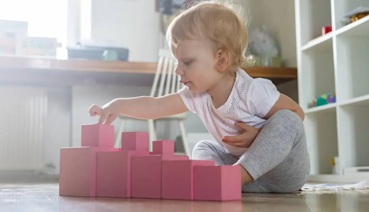 Bambina bionda gioca con blocchi rosa, ideali come giochi montessori 6 mesi fai da te per sviluppare la coordinazione.