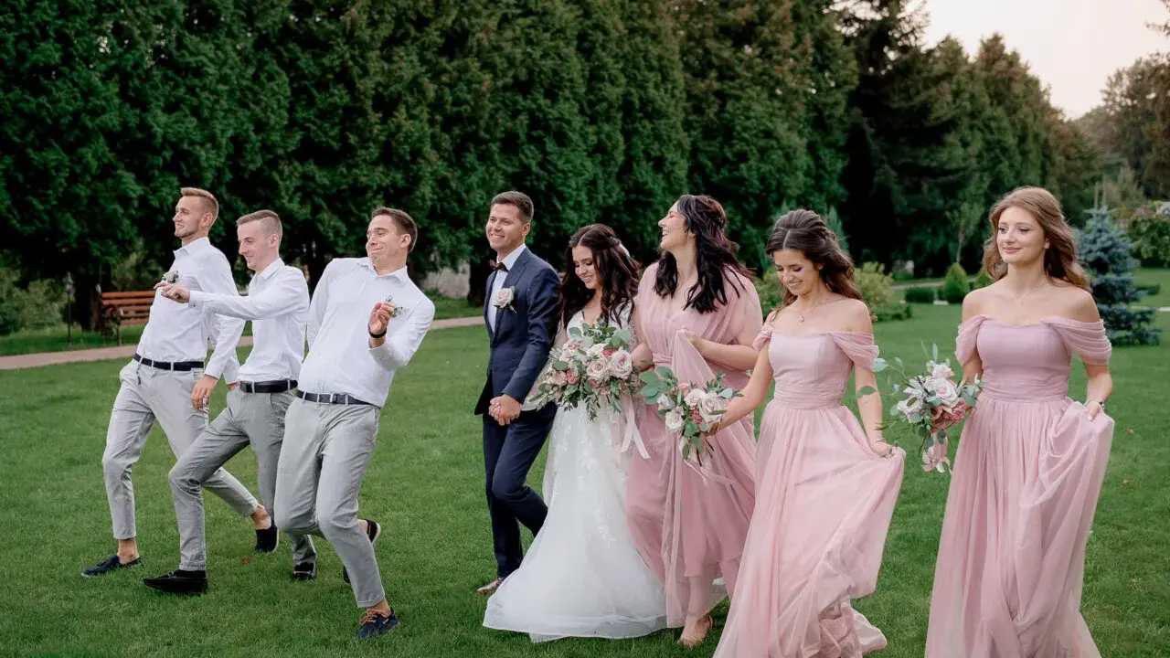 Para ślubna z drużbami i druhnami w eleganckim ubiorze na ślub, idący przez trawnik.