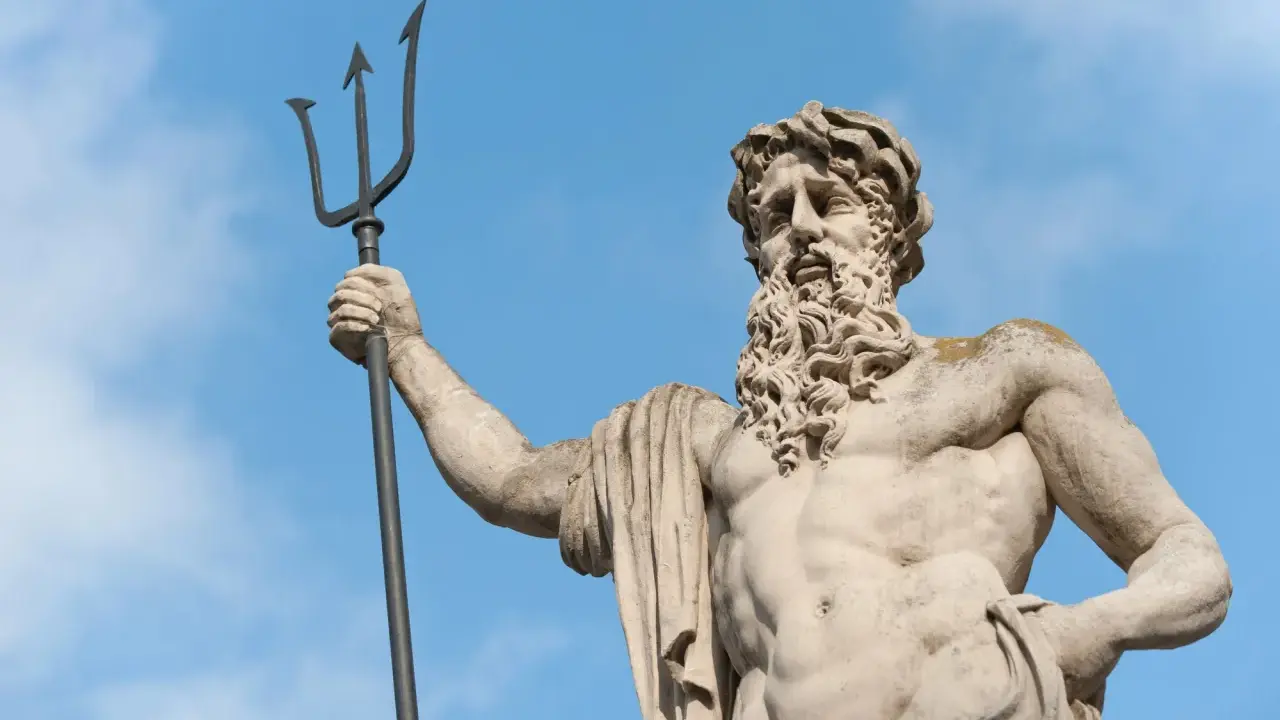 Statue de Poseidon dieu des mers, tenant son trident, sous un ciel bleu.