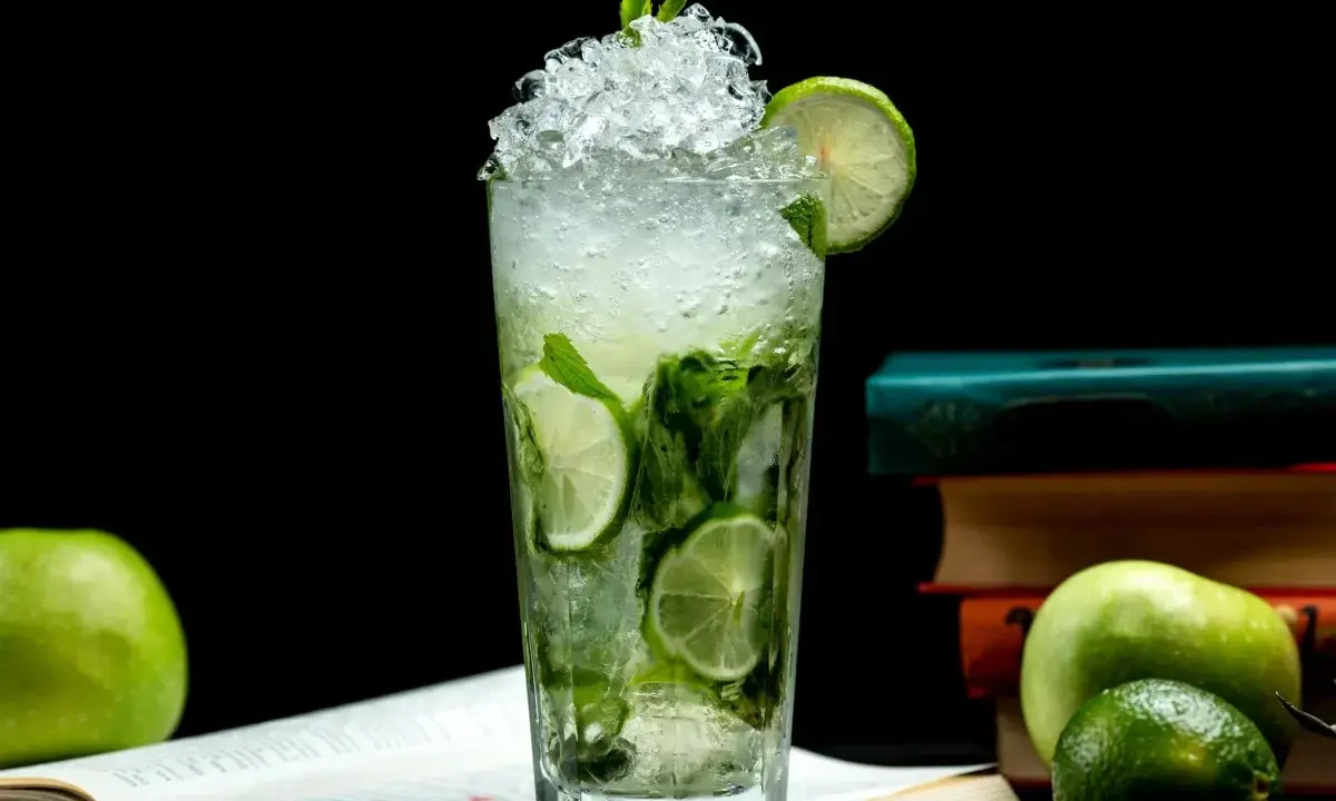 Orzeźwiający mojito przepis: szklanka pełna lodu, mięty i limonki, obok jabłka i książki. Idealny na letnie popołudnie.