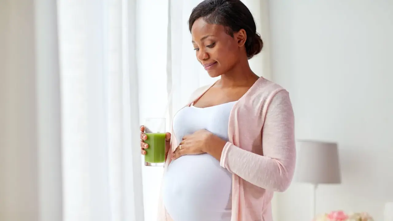 Femme enceinte tenant un verre de jus vert, caressant son ventre. Elle prend soin de sa peau sèche pendant la grossesse.
