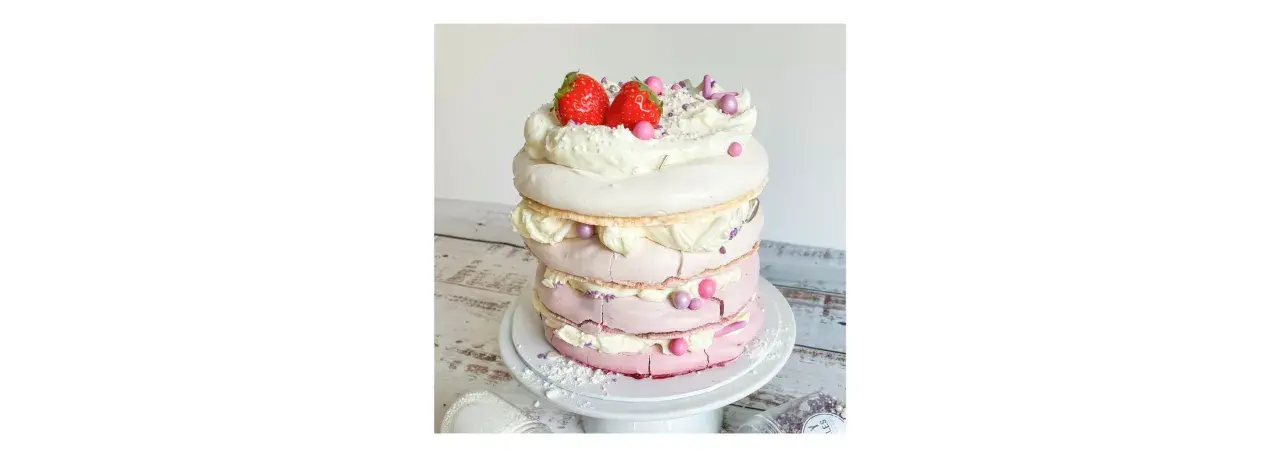 Eine mehrstöckige Baiser Torte mit Sahne, Erdbeeren und rosa Zuckerperlen.