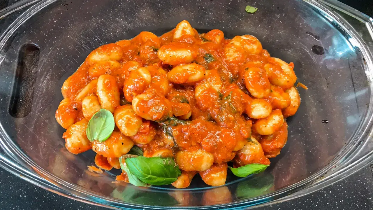 Pyszne gnocchi z sosem pomidorowym i świeżą bazylią, podane w szklanej misie. Idealne danie dla miłośników włoskiej kuchni.