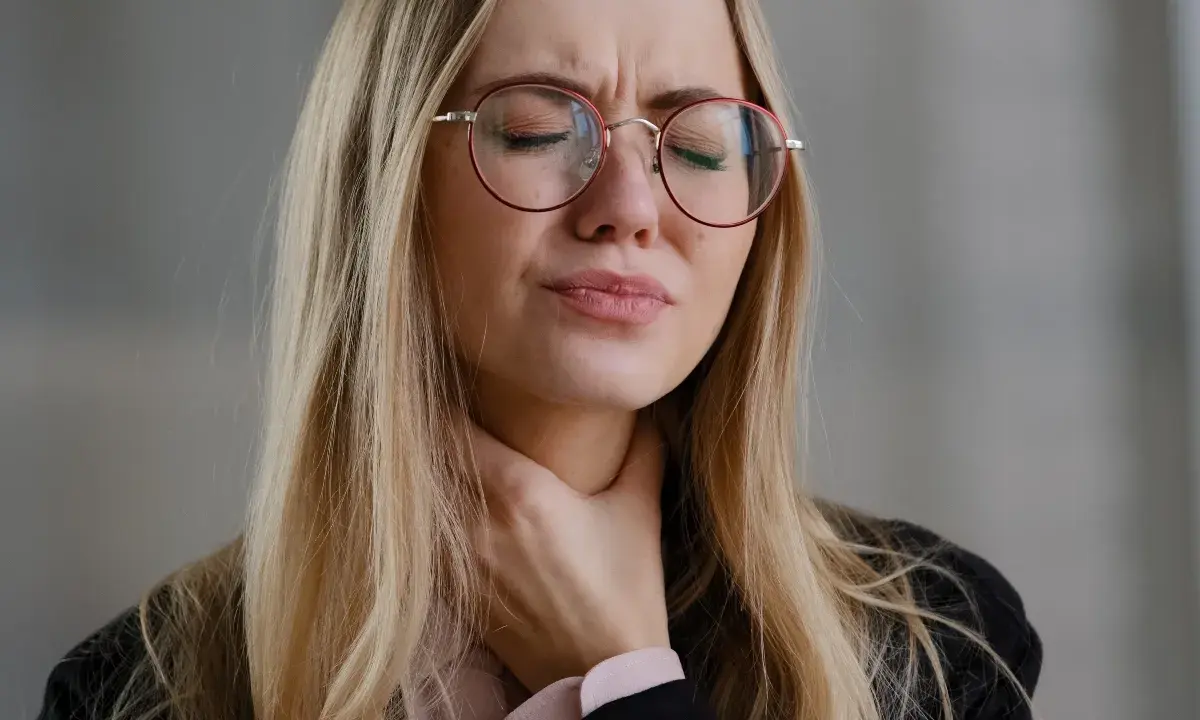 Donna con occhiali rossi si stringe la gola, visibilmente sofferente. Cerca rimedi per un prurito insopportabile.