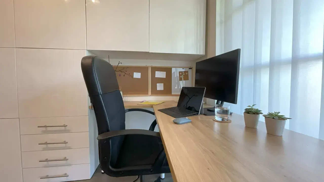 Un coin bureau moderne et fonctionnel pour aménager votre espace de travail. Chaise noire, bureau en bois, écran, ordinateur portable et plantes vertes.