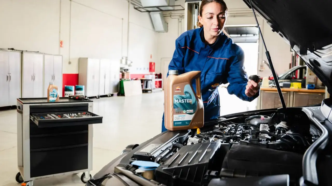 Mecánica muestra cómo cambiar el aceite del coche, sosteniendo una botella de aceite Repsol Master.
