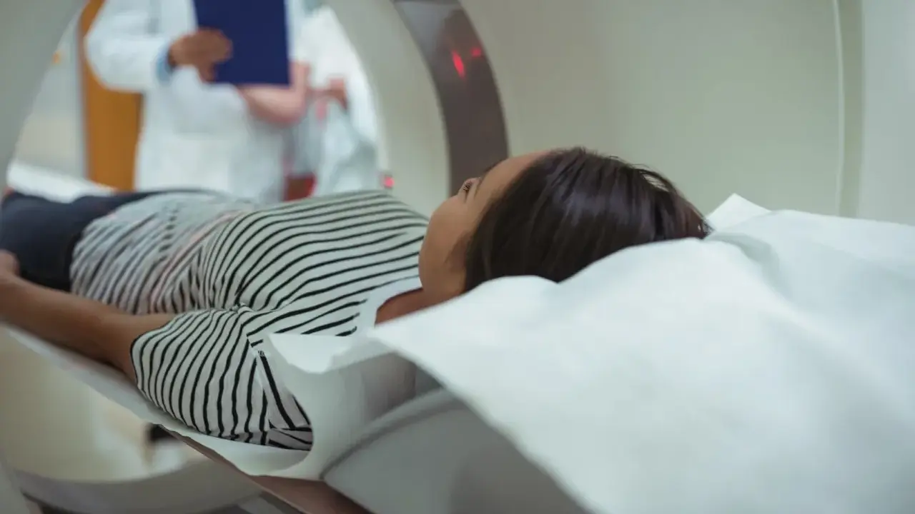Pacjentka leży na łóżku rezonansu magnetycznego, obok niej stoi lekarz z dokumentacją.