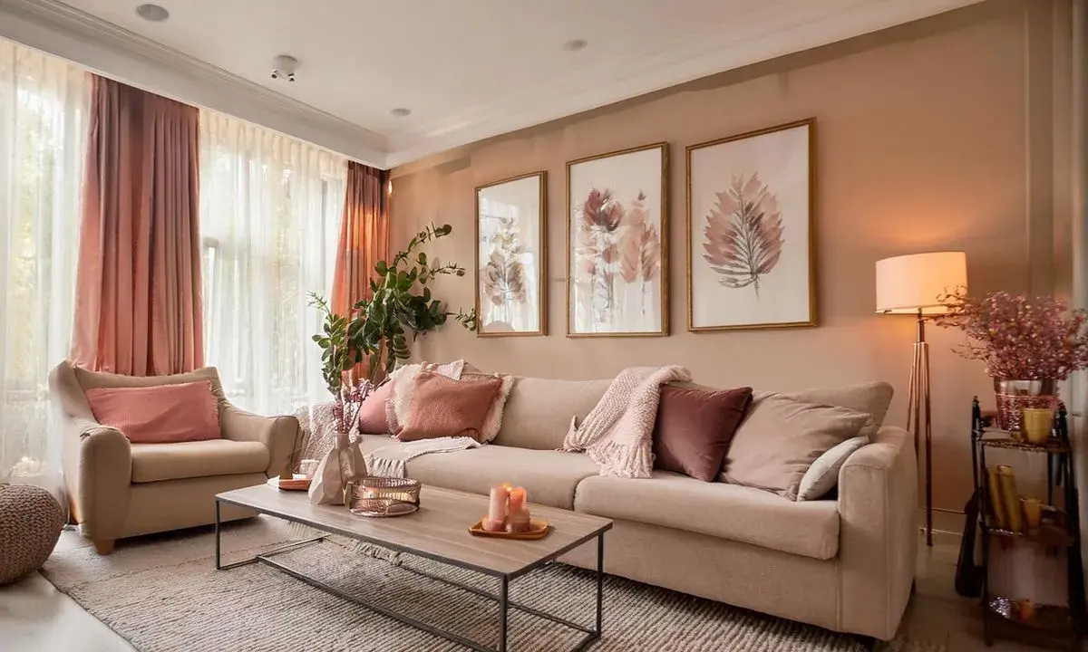 Un salon coloré et chaleureux, avec un canapé beige, des coussins roses et des tableaux de feuilles.