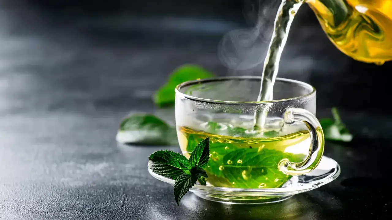 Un thé fumant à la menthe poivrée est versé dans une tasse transparente, ornée d'une feuille de menthe fraîche.