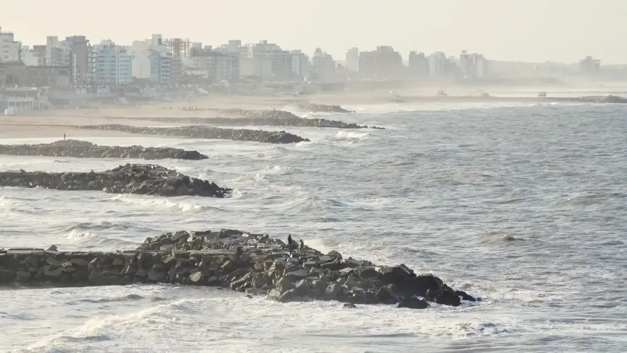 Olas rompen contra una escollera de rocas, protegiendo una ciudad costera. El escollera significado es claro: barrera contra el mar.