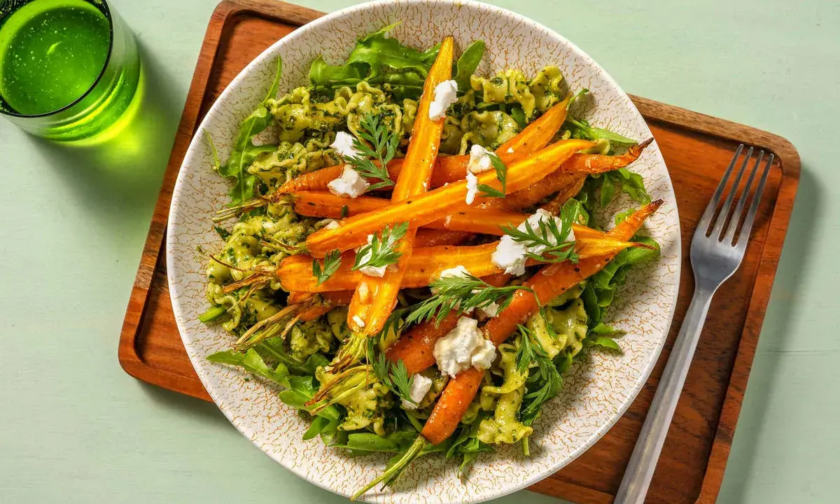 Pâtes vertes avec des carottes rôties et du fromage émietté, garnies de fanes de carottes fraîches.