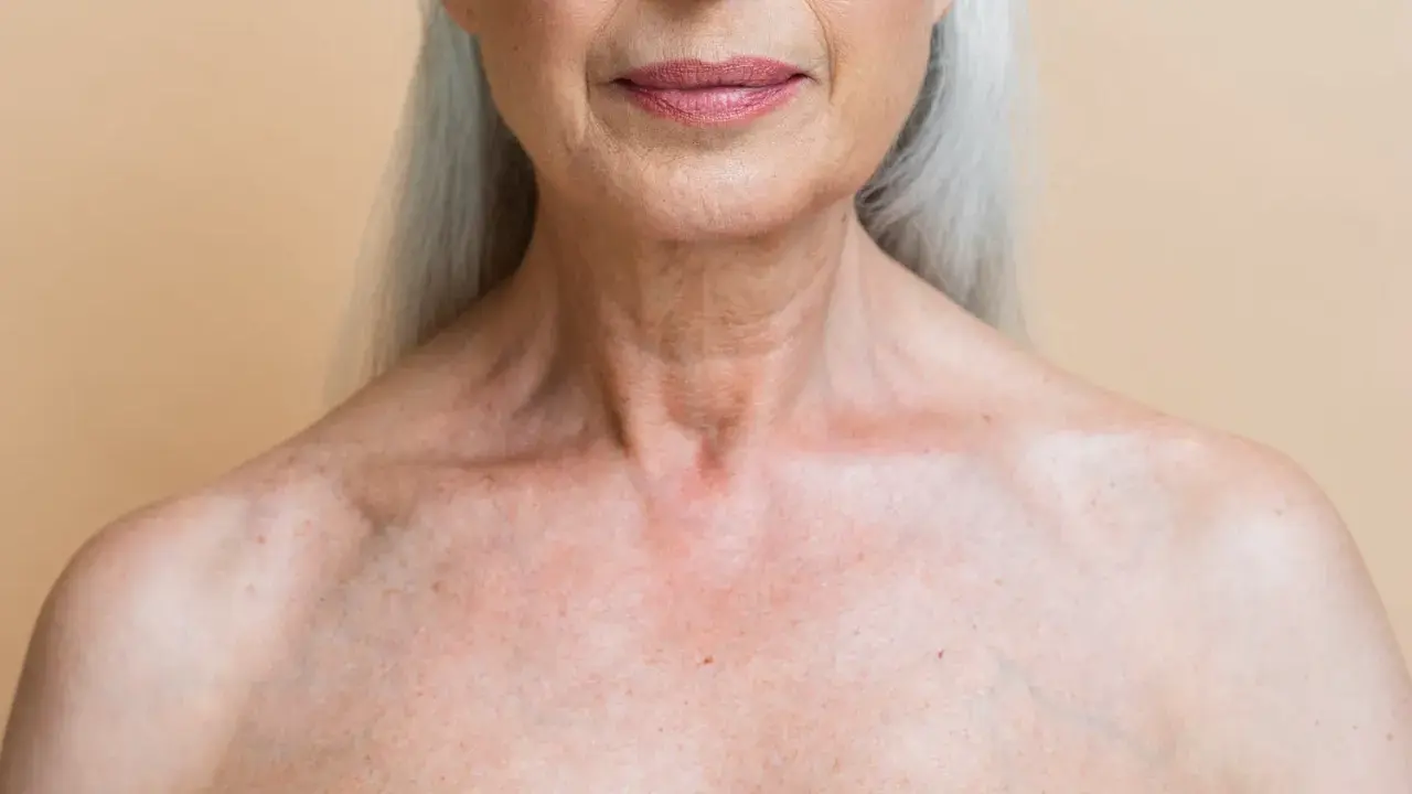 Gros plan sur le décolleté d'une femme âgée, montrant les marques du temps et les dégâts du soleil sur la peau.