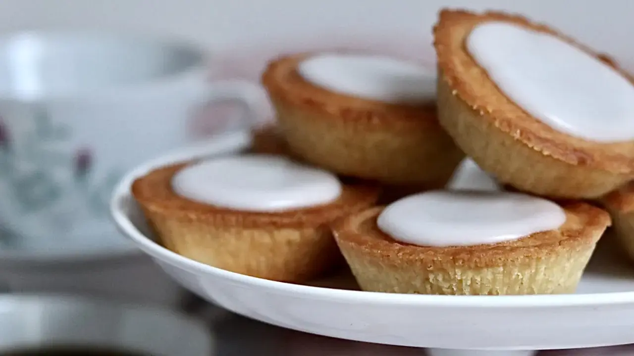 Små, gyllene mazariner med vit glasyr på ett tårtfat. Perfekt till fikat, här är ett enkelt mazariner recept.