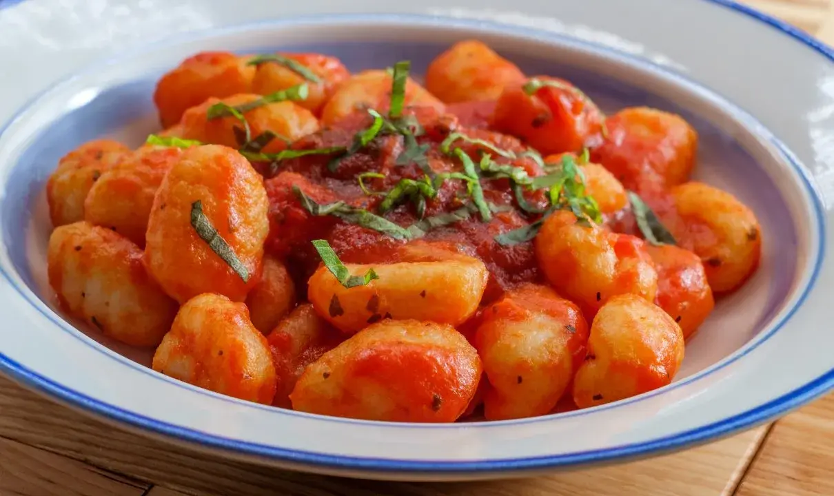 Pyszne gnocchi w sosie pomidorowym, posypane świeżą bazylią, podane w niebiesko-białej misce.