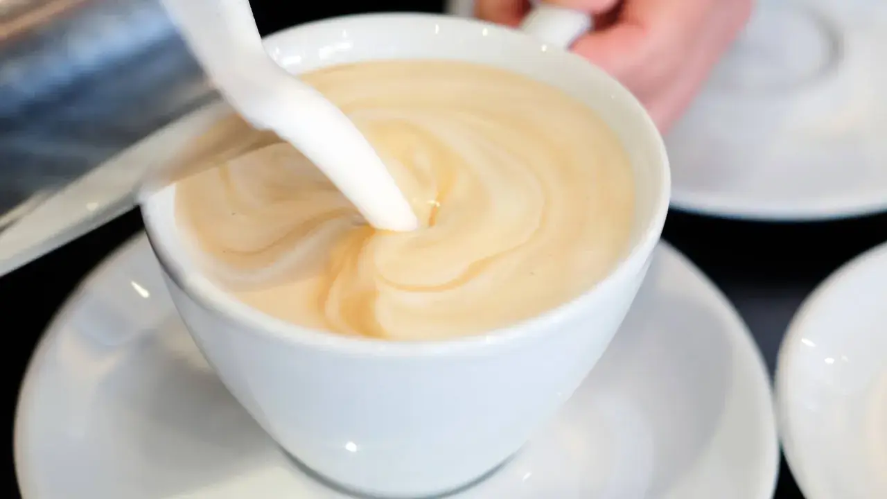 Milch wird in eine Tasse mit Kaffee gegossen, um ein cremiges Café au Lait zu kreieren.