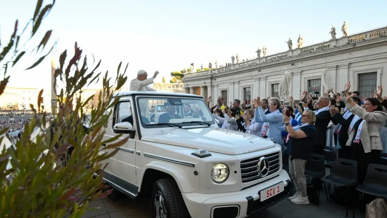 Papież Franciszek, mimo swojego vatican wiek, pozdrawia wiernych z białego mercedesa. Tłum wiwatuje, a niektórzy robią zdjęcia.