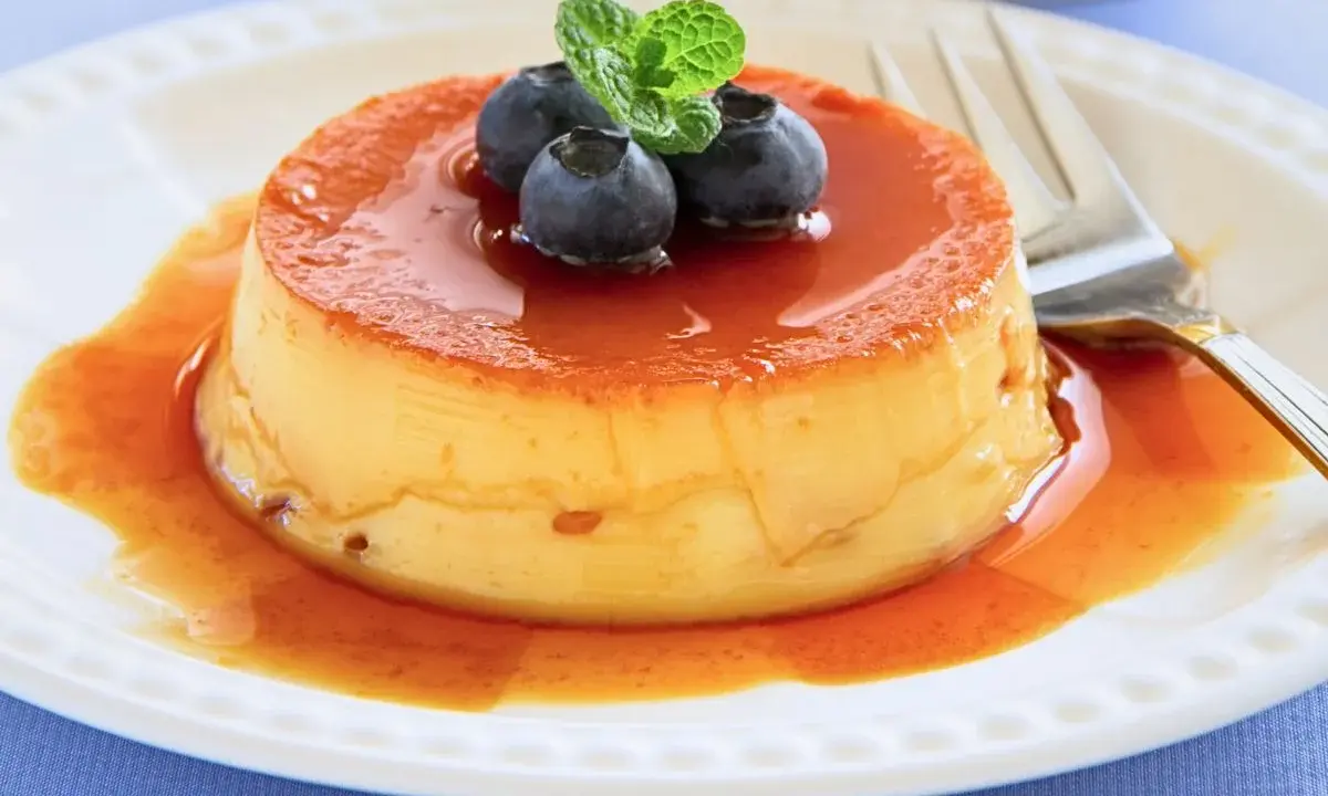 Delicioso flan de queso con cuajada, cubierto de caramelo líquido y adornado con arándanos y menta.