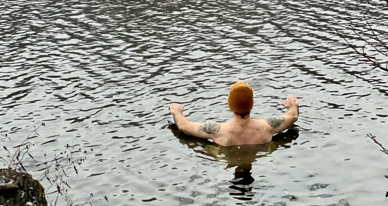 Man med orange mössa och tatueringar njuter av kallt bad i en sjö.