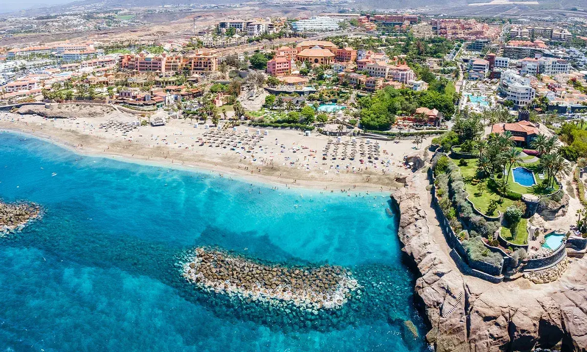 Widok z lotu ptaka na Costa Adeje plaże z turkusową wodą, piaszczystym brzegiem pełnym leżaków i palmami.