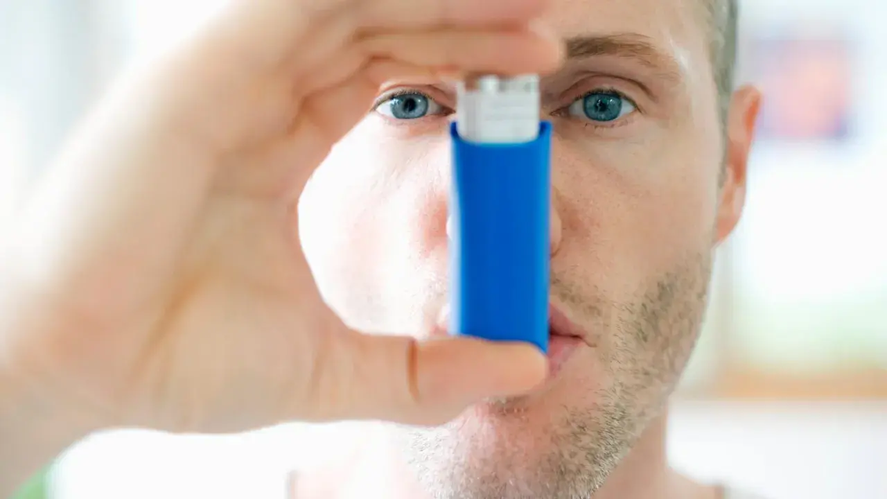 Mann mit blauen Augen hält einen blauen Inhalator, ein reliever asthma.