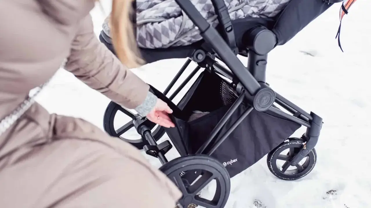 Kobieta wkłada coś do kosza wózka Cybex Priam. Waga wózka jest niewielka, co ułatwia manewrowanie w śniegu.