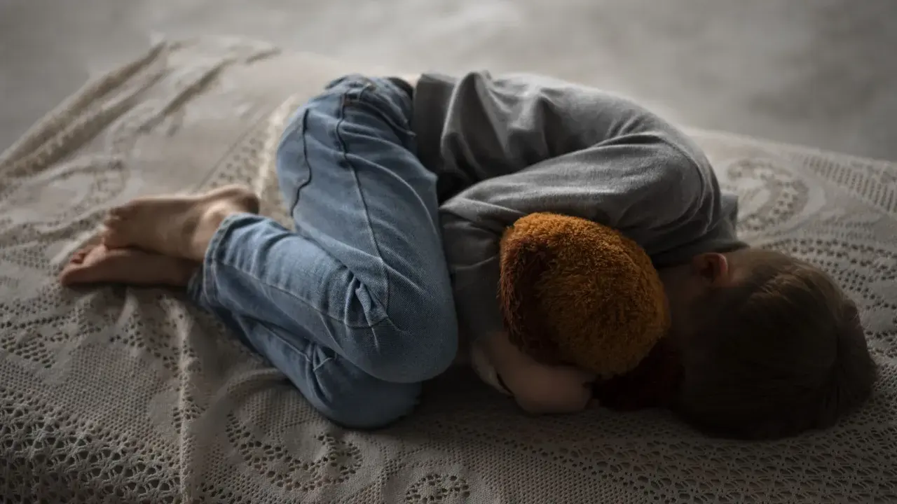 Un niño abraza un peluche, acurrucado en una cama. Una imagen que evoca la necesidad de saber como explicar la muerte a un niño.