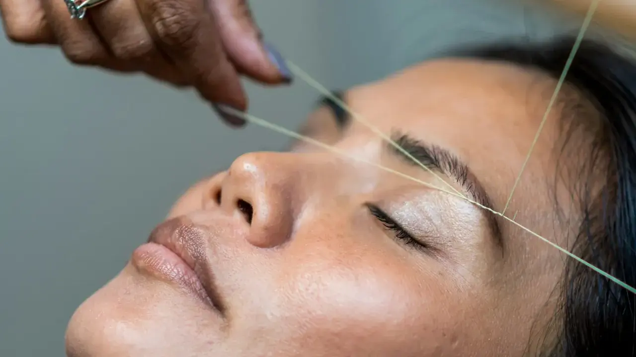 Une main experte réalise un rehaussement sourcils avec du fil. La précision du geste promet un regard sublimé.