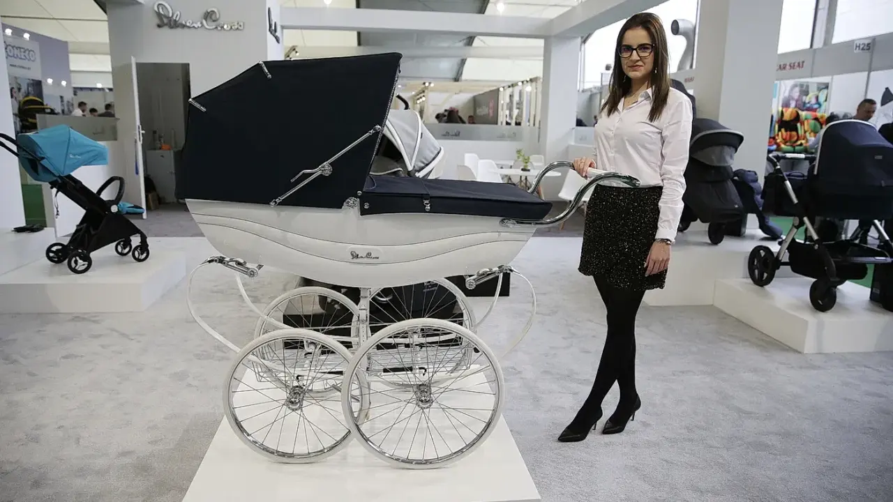 Elegancka kobieta prezentuje najdroższe wózki dziecięce, w tym luksusowy model Silver Cross z białym koszem i czarną gondolą.