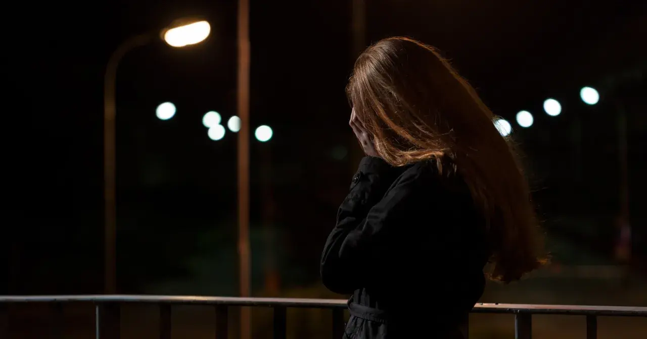 Kobieta z rudymi włosami, zakrywająca twarz dłońmi, stoi na balkonie nocą. W tle migoczą światła uliczne, symbolizujące stres przed seksem.
