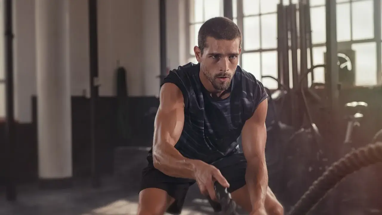 Ein Mann trainiert mit Seilen im Fitnessstudio. Das ist funktionelles Training, das Kraft und Ausdauer verbessert.