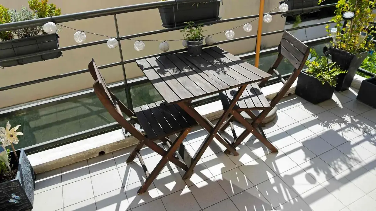 Un piccolo tavolo e sedie in legno su un balcone, con piante e lucine, perfetti per trasformare il balcone in terrazzo.