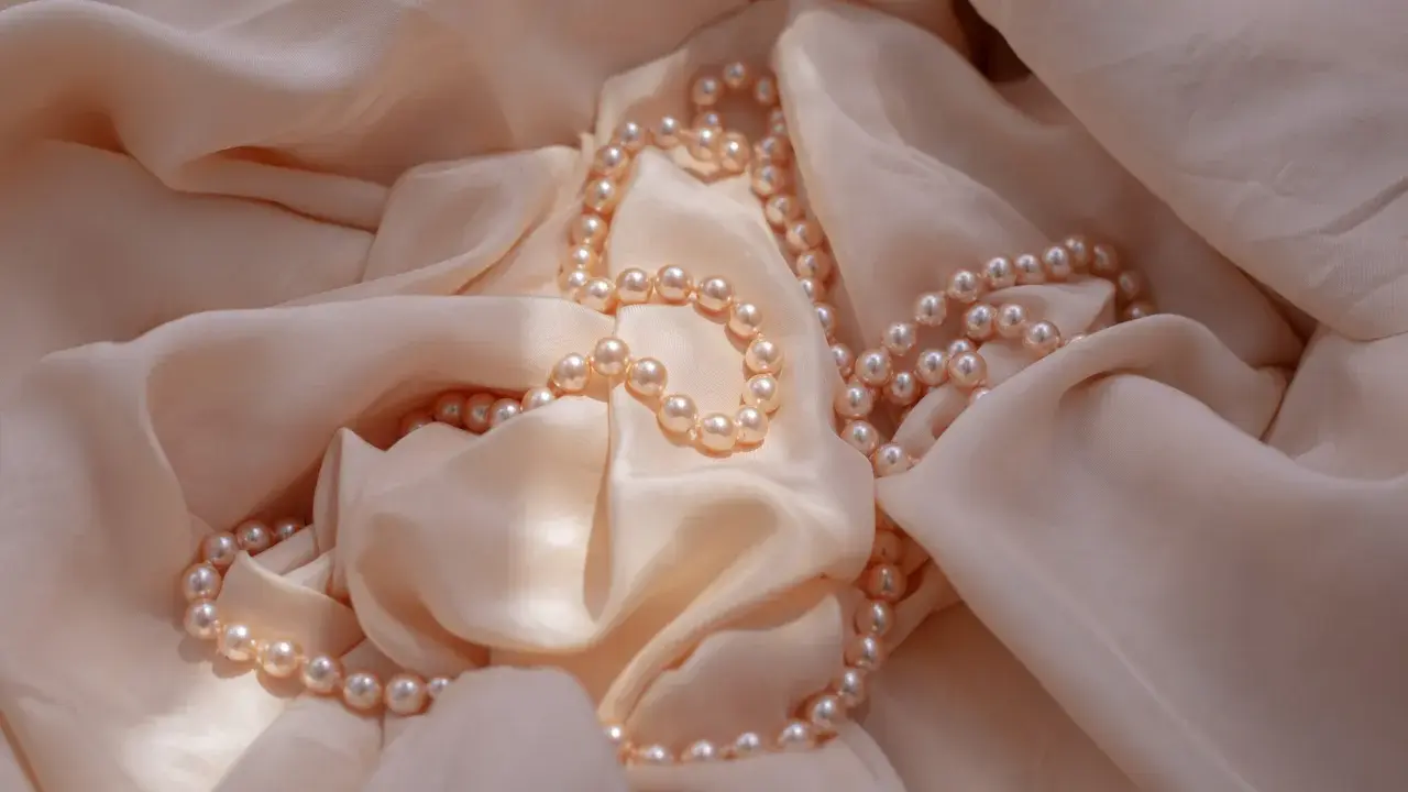 Un filo di perle rosa pallido adagiato su una morbida seta color crema. Un'idea perfetta per regalare perle.