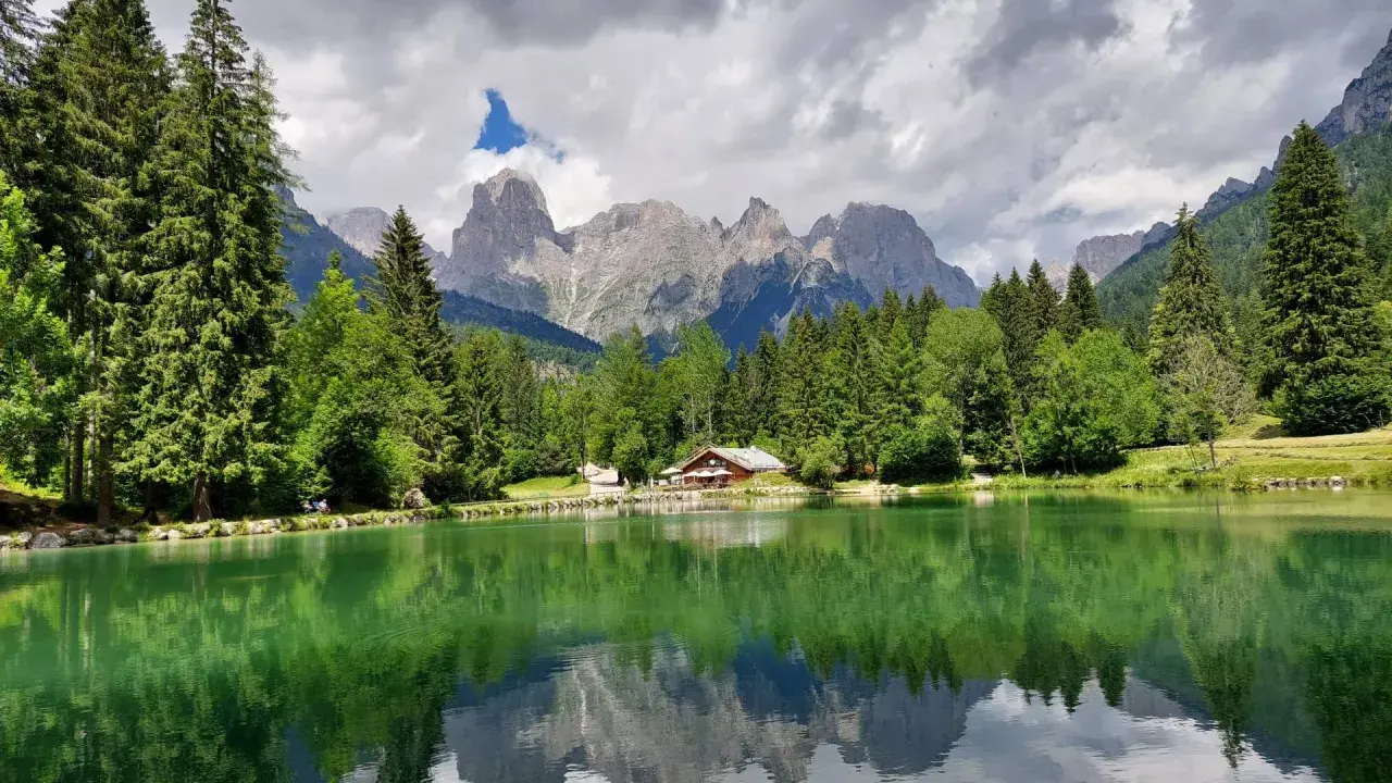 Riflessi perfetti sul lago Welsperg, con montagne maestose e una baita accogliente tra gli alberi.