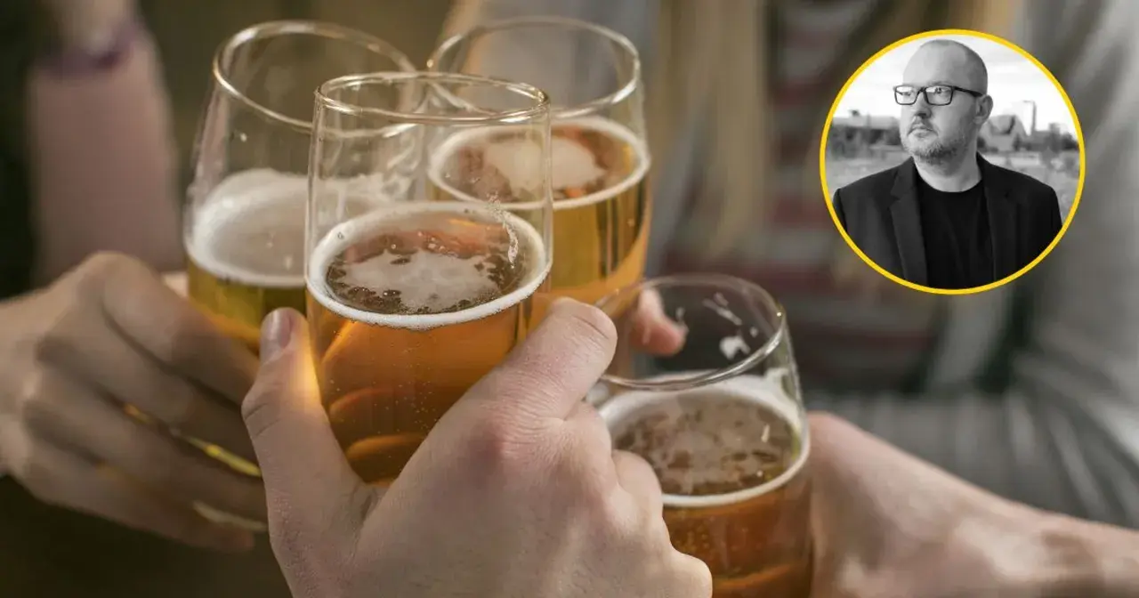 Ludzie wznoszą toasty piwem, podczas gdy w tle widać mężczyznę w okularach, który może symbolizować problem z alkoholem.