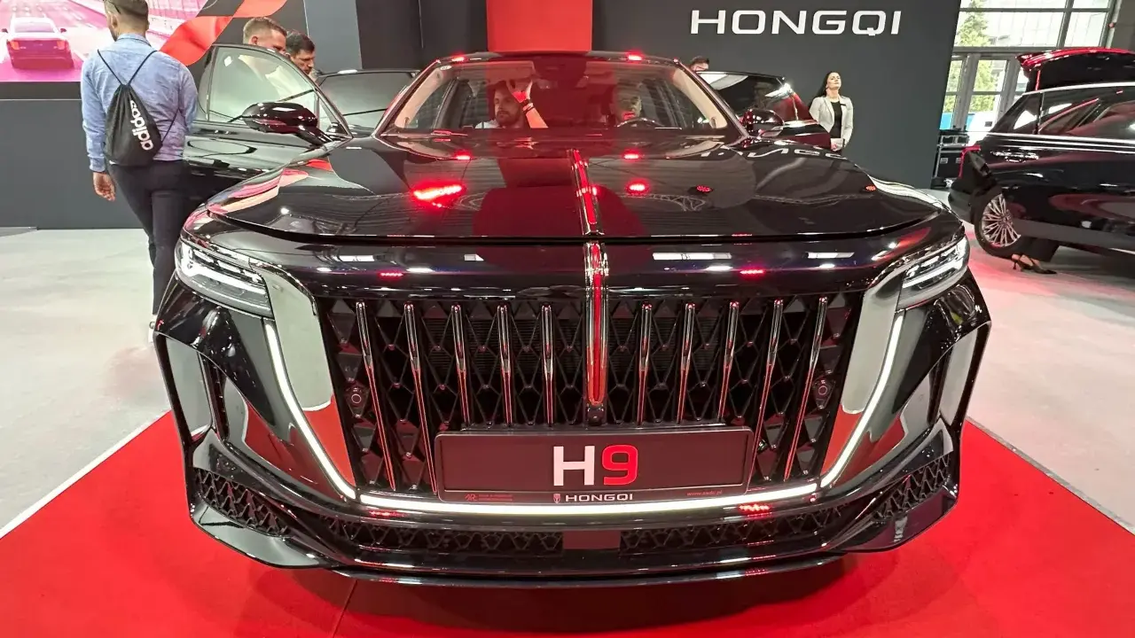 Elegancki czarny Hongqi H9 z chromowanym grillem i czerwonymi akcentami. Zainteresowani sprawdzają jego cenę na wystawie.