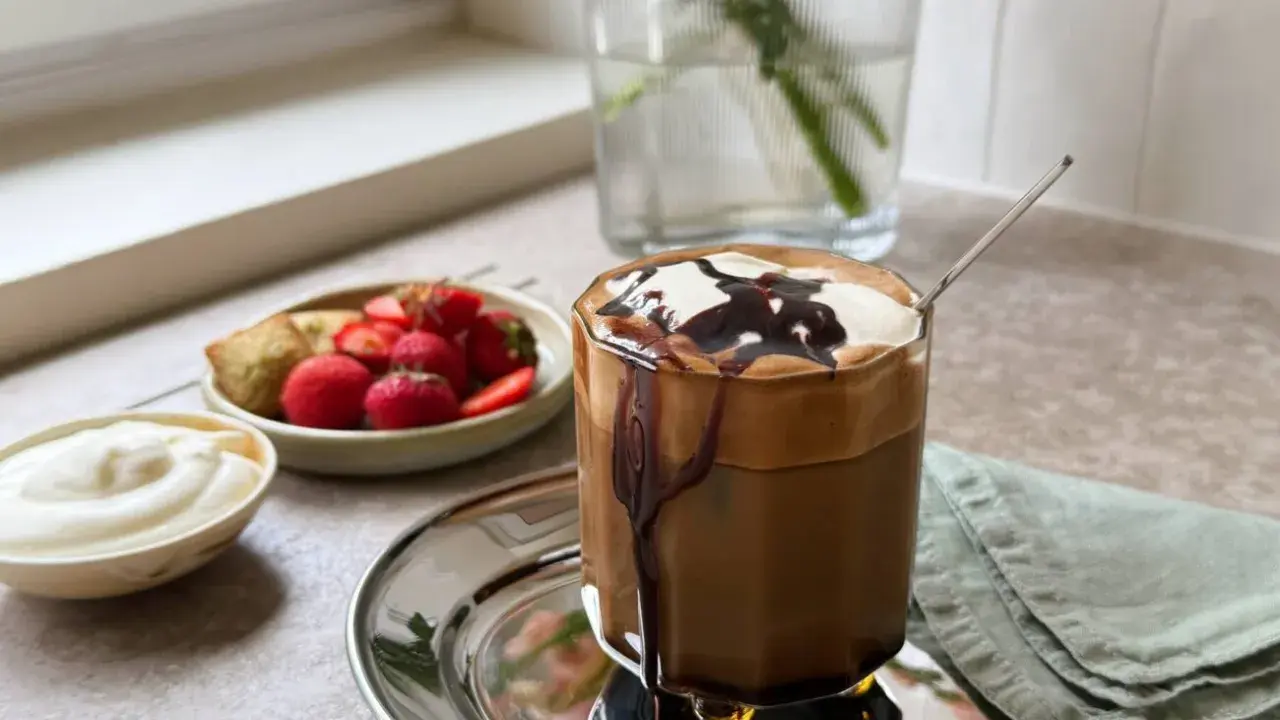 En läcker frappe med chokladsås och grädde, serverad med färska jordgubbar och en bit bakverk. Ett perfekt frappe recept för en solig dag.
