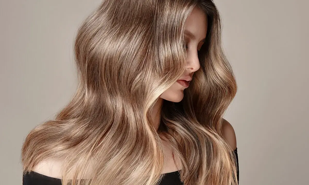 Mujer con cabello largo y ondulado, con un degradado de castaño a rubio. Un ejemplo de cómo aclarar el pelo teñido para un look natural.