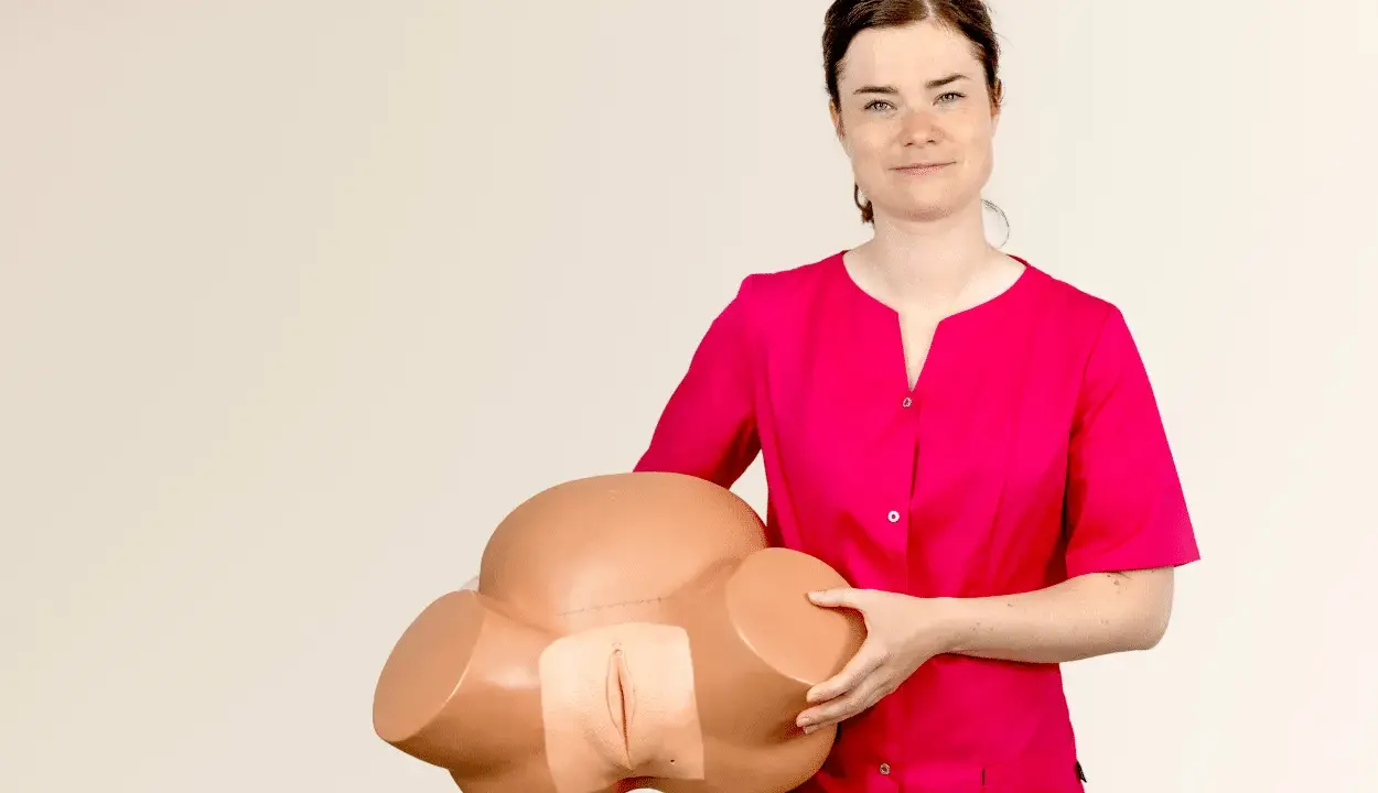 Kobieta w różowej bluzce trzyma model miednicy, demonstrując anatomię do nauki masażu szyjki macicy.
