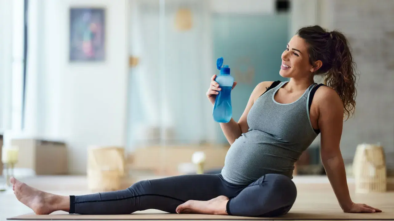 Donna incinta sorride con una bottiglia d'acqua dopo una sessione di yoga in gravidanza.