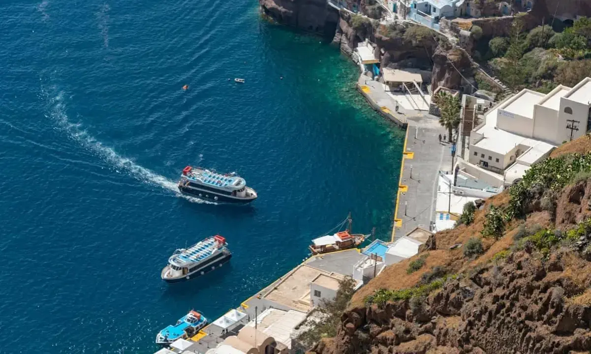 Barche turistiche navigano nel blu intenso del porto di Santorini, con le case bianche aggrappate alla scogliera.