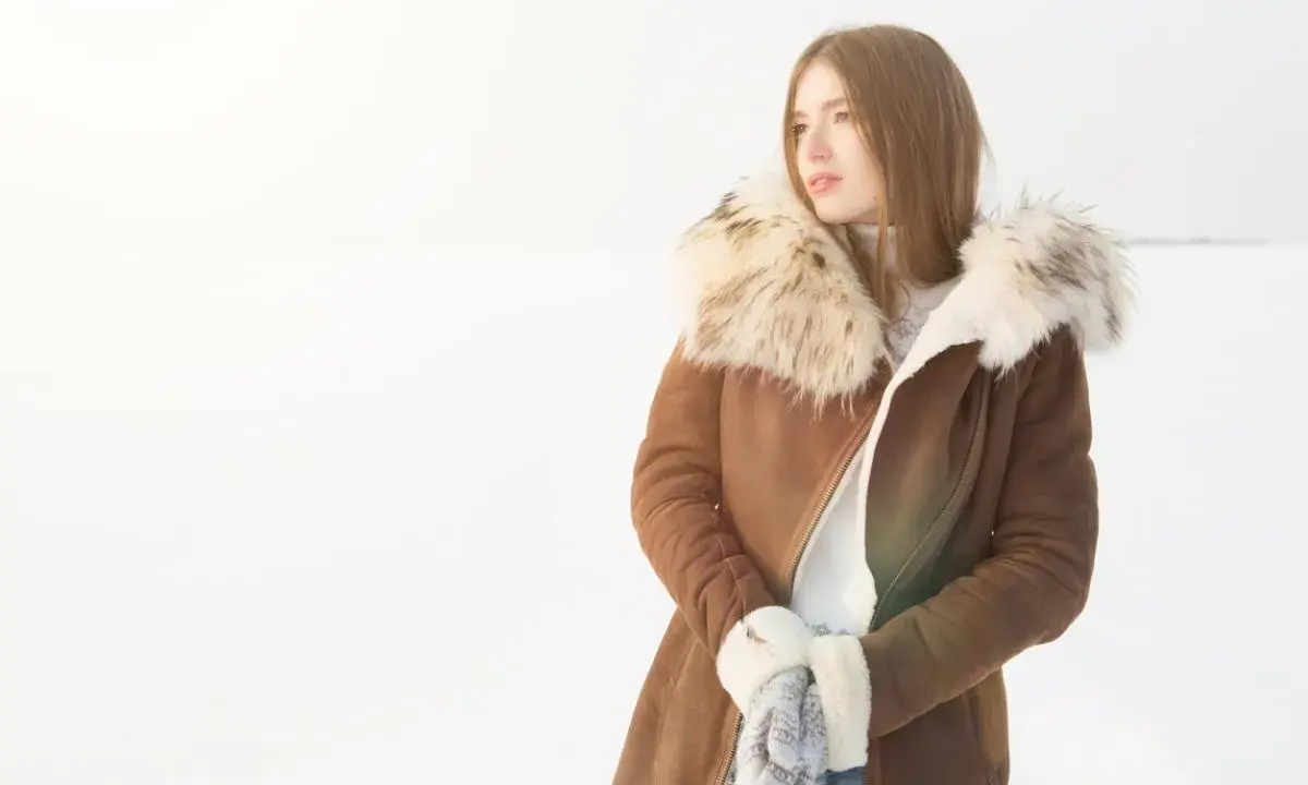 Mujer con abrigo de pelo natural en la nieve, lista para limpiar su ropa de invierno.