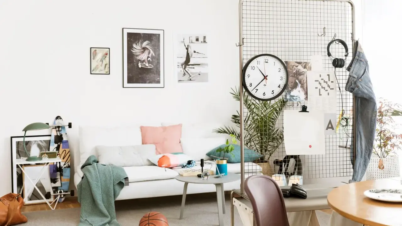 En avslappnad inredning hemma med vit soffa, konst på väggen, en basketboll och en skateboard. En stor klocka hänger på ett metallgaller.