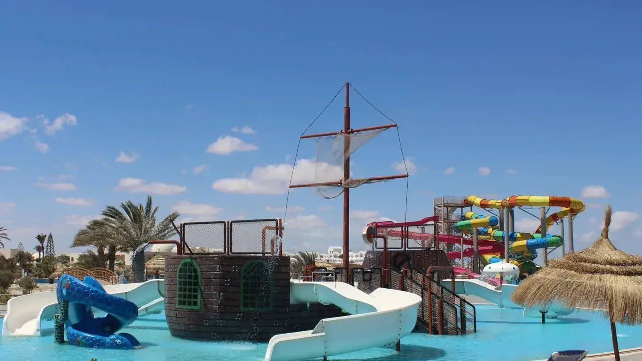 Djerba Aqua Resort (ex. Sun Connect) z pirackim statkiem i kolorowymi zjeżdżalniami wodnymi pod błękitnym niebem.