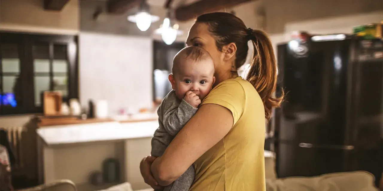 Zmęczona mama tuli dziecko, szukając sposobu, jak oduczyć dziecko jeść w nocy.