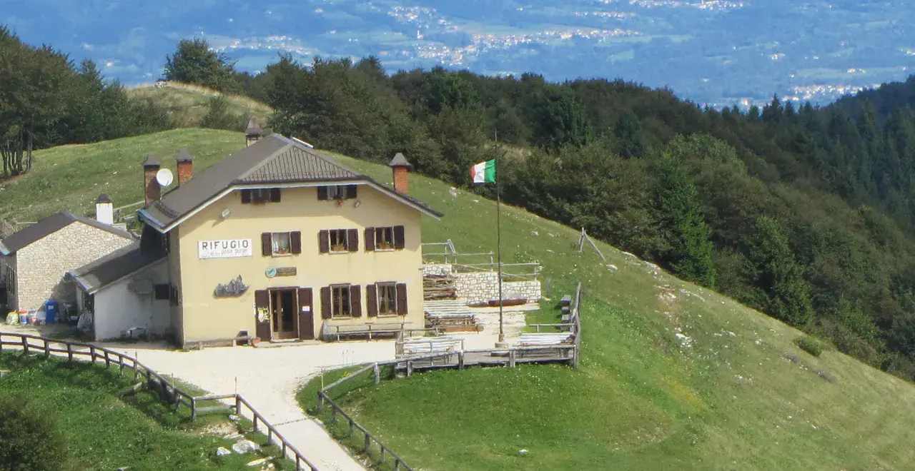 Il rifugio Posa Puner, con la bandiera italiana che sventola, domina un paesaggio montano verdeggiante.