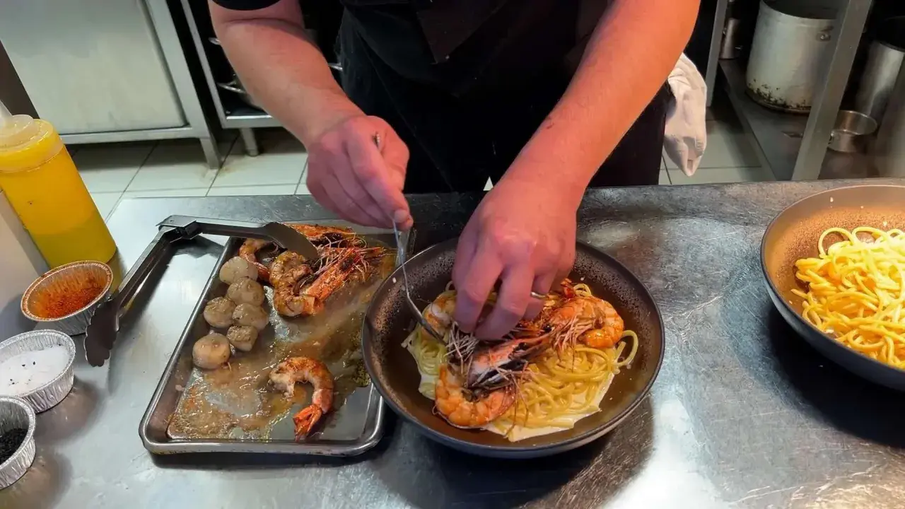 Un chef prépare des pâtes aux crevettes et pétoncles, un plat savoureux de cuisine de terroir.