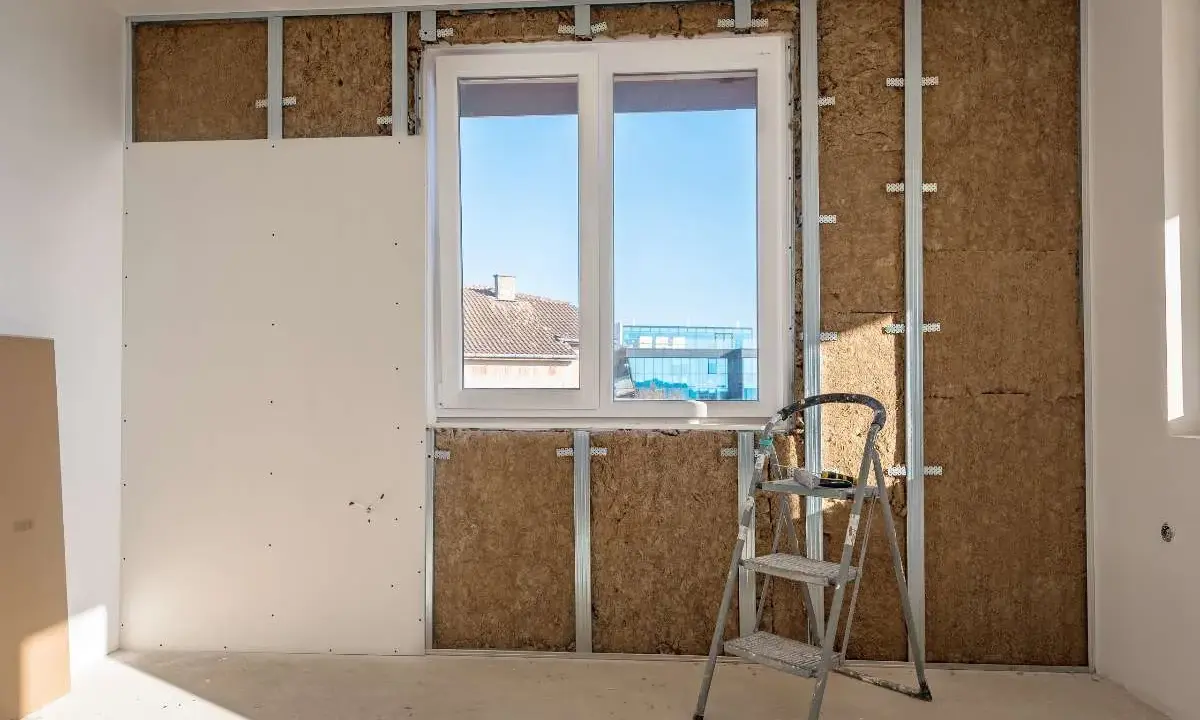 Instalación de un trasdosado de pladur con aislamiento, mostrando la estructura metálica, la lana de roca y una placa de yeso.
